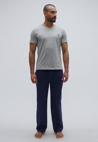 Szara koszulka z okrągłym dekoltem, mieszanka bawełny, z małym logo; zestawiona z granatowymi spodniami do relaksu, o prostym kroju, z lekkiego materiału, bez widocznych wzorów.