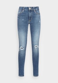 Jeans ajustados en denim azul claro, con roturas desgastadas en las rodillas, una textura ligeramente desvanecida y un diseño clásico de cinco bolsillos con un botón de metal.
