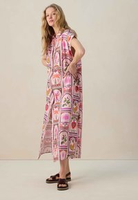 Robe ample à motifs floraux roses avec des manches courtes, présentant divers motifs et des couleurs vives, associée à des sandales noires.