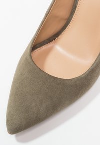 Chaussure femme à bout pointu en daim vert olive avec doublure intérieure en cuir beige, vue de dessus sur fond blanc.
