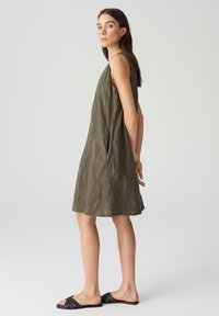 Khaki sleeveless dress with textured leaf pattern, relaxed A-line shape, and side pockets. Worn with black flat sandals.