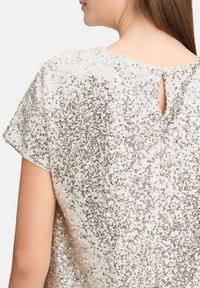 Pailletten top in zilveren en gouden tinten, korte mouwen, een keyhole-detail aan de achterkant met een knoopsluiting, glinsterende textuur overal.