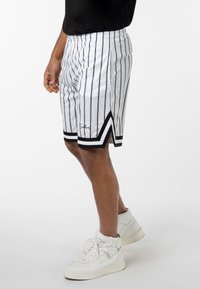 White athletic shorts with black vertical stripes, featuring a black accent at the hem and a v-shaped cut on the sides.