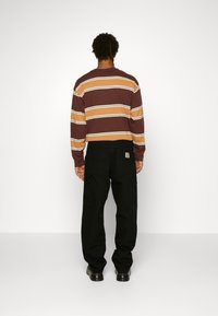 Camisa de rayas marrón de manga larga con líneas amarillas y blancas, combinada con pantalones cargo negros y zapatos negros, vista desde la parte de atrás.