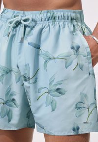 Pantaloni scurți de înot albastru deschis cu model floral, realizați dintr-un material ușor. Prezintă o talie elastică cu șnur și buzunare laterale.