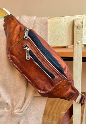 Marsupio in pelle marrone con finitura testurizzata, tasca con zip e tracolla regolabile. Forma rettangolare con zip nera a contrasto.