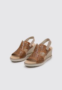 Sandalias de cuña de cuero marrón con patrones cortados, diseño de punta abierta, correa ajustable en la parte trasera y suela de goma beige.
