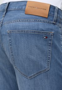 Πίσω μέρος μπλε τζιν με δερμάτινη ετικέτα Tommy Hilfiger και μικρό κόκκινο, λευκό και μπλε λογότυπο στην τσέπη.