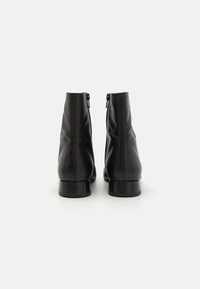 Botas de cuero negras hasta el tobillo con una textura suave, cierres de cremallera en la parte trasera y tacones bajos resistentes, con un diseño minimalista.