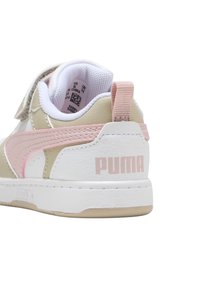 Sneaker bianco e beige con dettagli rosa, dotata di una fascetta in Velcro, pannelli testurizzati e un logo posteriore su una suola in gomma.