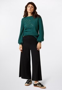 Teal knitted sweater with textured pattern, black wide-leg trousers, and black sneakers with cream stripes. Relaxed fit, long sleeves.