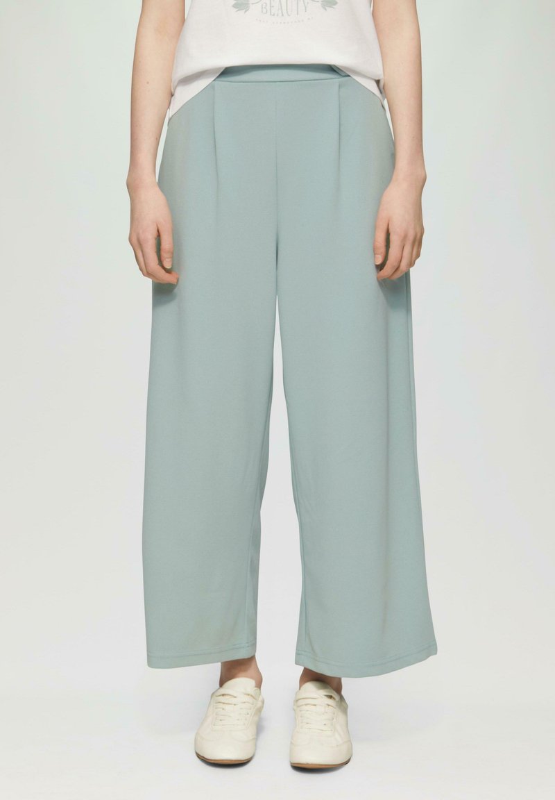 Lichtblauwe wijde broek van zachte stof, met plooien aan de voorkant en een elastische tailleband, gecombineerd met witte sportschoenen.