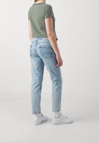 Camiseta de tiro corto a rayas verdes y blancas combinada con jeans rectos de tiro ligero en azul. Zapatillas blancas completan el atuendo. Textura suave.