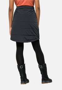 Zwarte, geïsoleerde skort met gelaagde stiksels, een gebogen zoom en een hoge tailleband, gecombineerd met zwarte panty's en enkellaarsjes.