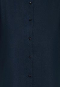 Camicia button-up di un blu navy scuro con tessuto strutturato. Presenta sei bottoni neri sul davanti, con un design del colletto classico.