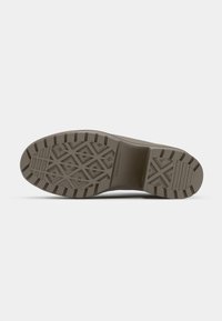 Shoe sole with a textured, geometric pattern, primarily in light brown rubber, featuring grooves for traction and branding details.