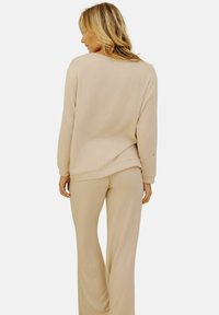 Ensemble lounge beige comprenant un haut à manches longues à coupe décontractée et un pantalon à jambes larges en matière douce et texturée. Design simple avec des accents minimalistes.