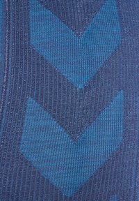 Texturerad tyg med en marinblå bakgrund och framträdande teal chevronmönster. Designen är stickad med fina horisontella ränder.