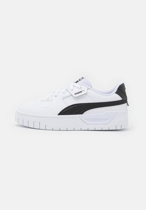 Sneaker blanche avec des accents noirs, présentant un dessus en cuir lisse, une pointe arrondie, une semelle épaisse avec un motif nervuré et des détails de marquage.