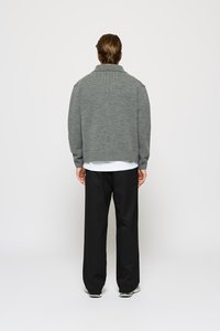 Grauer Strickpullover mit Kragen, der einen lässigen Schnitt hat. Über einem weißen Hemd getragen und mit schwarzen weit geschnittenen Hosen kombiniert.