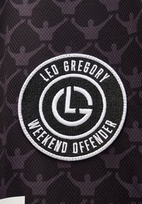 Tessuto nero con un motivo di figure umane. Toppa ricamata circolare con "LED GREGORY" e "WEEKEND OFFENDER" in testo bianco.