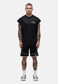 Zwarte sportoutfit bestaande uit een short-sleeve, loszittend shirt en bijpassende shorts met witte accenten, gemaakt van lichte stof.