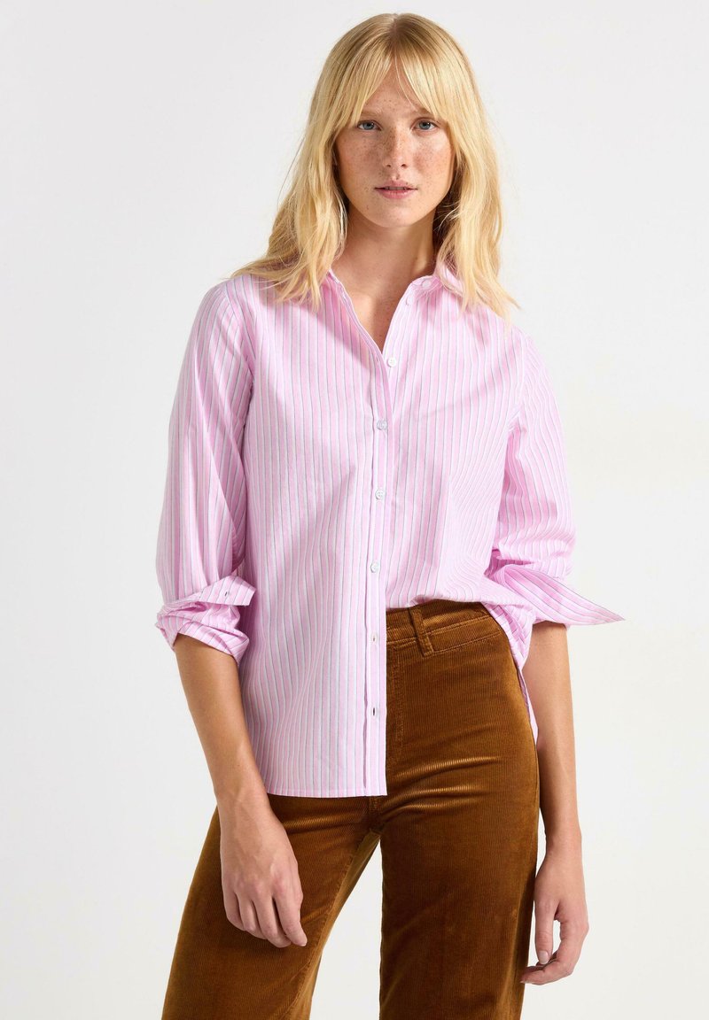 Lyserød skjorte med knapper og fine blå og hvide striber, optrukne ærmer og lige snit. Sammen med brune kordfløjl bukser.