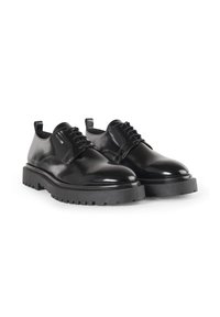 Scarpe in pelle nera con finitura lucida, punte arrotondate e una suola in gomma spessa e striata. Presentano lacci e un piccolo manico sul tallone.