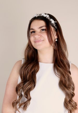 Coroncina floreale con fiori bianchi e perline trasparenti, indossata con lunghi capelli castani ondulati. Modella in un vestito bianco senza maniche. Sfondo semplice.