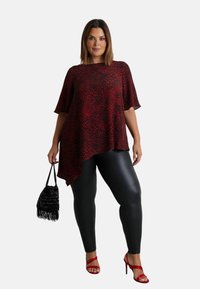 Top s leopardím potiskem v červené a černé barvě s asymetrickým lemem, doplněný černými legínami z umělé kůže a červenými sandály na vysokém podpatku. Černá kabelka.