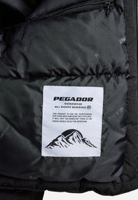 Fekete puffers jacket belső, fehér címkével, rajta "PEGADOR" felirattal, hegyrajzzal és fekete színű ápolási utasításokkal. Simas textura.
