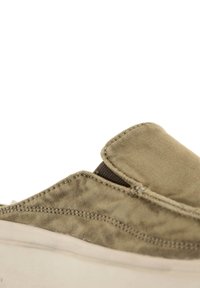 Zapatillas de tela tipo slip-on en verde olivo con un upper de tejido texturizado, acentos en marrón contrastante y suela de goma de color claro.