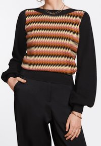 Pull tricoté avec un motif géométrique dans des nuances de rose, de marron et de crème sur le devant, manches et bas noirs, poignets côtelés.