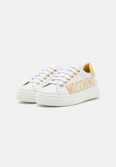Baltos odinės sneaker'iai su auksiniais akcentais, ypač auksinės akių skylės ir "MOSCHINO" blizgiu ant šono. Lygus guminis padas, suapvalinta nosis.