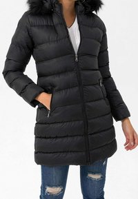 Sort pufferjakke med lynlås foran, vandret syninger og en faux fur hætte. To sidelommer fuldender designet.