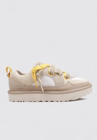 Zapatilla baja de ante beige y blanca con suela gruesa, tirador en forma de bucle amarillo y cordones amarillos y beige.