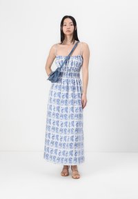 Abito lungo in tessuto bianco con fantasie floreali blu, con busto arricciato, spalline sottili e una vestibilità comoda. Indossato con una piccola borsa blu.