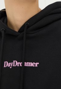 Czarna bluza z kapturem z różowym nadrukiem "DayDreamer". Posiada kaptur ze ściągaczem oraz miękką, strukturalną tkaninę.