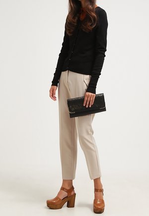 Svart långärmad cardigan, beige tapered byxor med framseams, bruna plattformsskor och en svart clutch med en texturerad design.