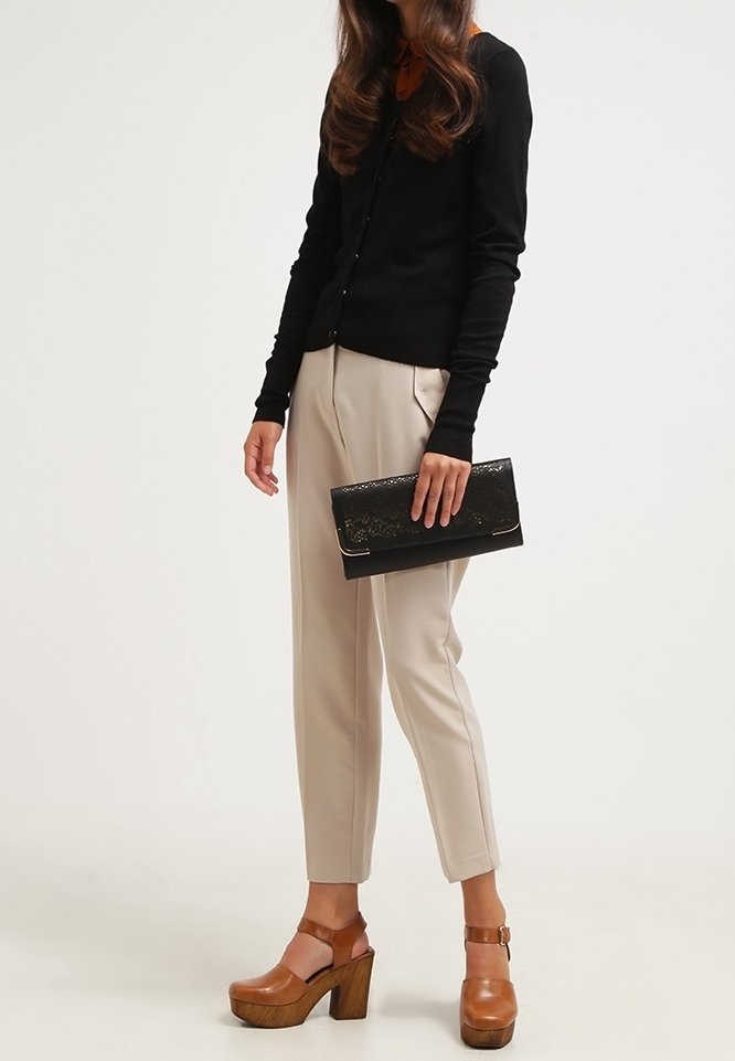 Svart långärmad cardigan, beige tapered byxor med framseams, bruna plattformsskor och en svart clutch med en texturerad design.
