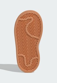 Semelle de chaussure en caoutchouc avec une texture ondulée de couleur brun clair, présentant un motif de design distinctif et des bords arrondis pour une meilleure adhérence et confort.