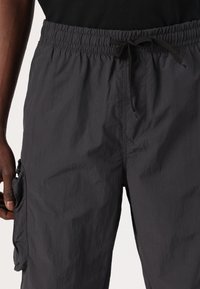 Calções cargo leves pretos com um cós elástico e cordão. Apresenta um bolso lateral com fecho de correr. Tecido texturizado.