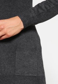 Ciemnoszary sweter z prążkowymi mankietami i małą przednią kieszenią. Tkanina wydaje się miękka i fakturowana, odpowiednia do codziennego noszenia.