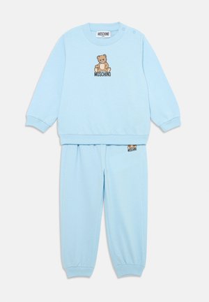 Ensemble en sweat-shirt et pantalon bleu clair, fabriqué en tissu doux. Présente un graphique d'ours et le logo "Moschino", avec des poignets et une taille côtelés.