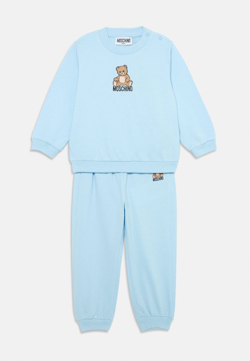 Conjunto de sweatshirt e calças azul claro, feito de tecido suave. Apresenta uma gráfica de urso e o logótipo "Moschino", com punhos e cintura canelados.