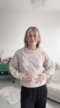 Maglione lavorato a maglia con schema di colori rosa chiaro e bianco, caratterizzato da motivi a trecce, scollatura arrotondata e polsini e orlo a coste.