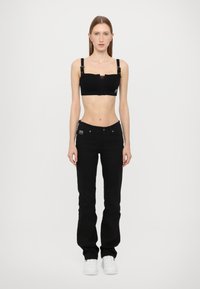 Black crop top with adjustable straps and a sheer panel; paired with fitted black jeans and white sneakers. Simple, modern design.