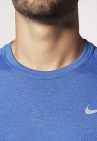 Niebieska koszulka sportowa wykonana z lekkiego materiału, z okrągłym dekoltem i małym odblaskowym logo Nike na piersi.