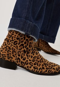 Stivali alla caviglia con stampa leopardata in morbido camoscio, con punta affusolata e tacco basso. Indossati con jeans di denim scuri, risvoltati alla caviglia.