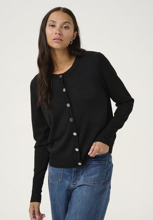 Cardigan en tricot noir avec un col rond, bouton sur le devant et poignets côtelés. Le tissu a un léger éclat. Associé à un jean en denim.